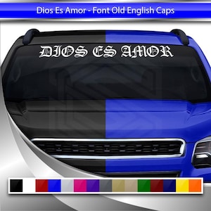 Op de afbeelding: Witte vinyl sticker met de tekst "DIOS ES AMOR" in Old English lettertype, ontworpen voor autoruiten. De sticker wordt weergegeven op een blauw en zwart voertuig. Een kleurenpalet wordt onderaan getoond.