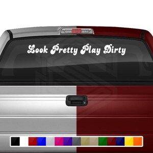 May include: A white decal with the text "Look Pretty Play Dirty" in a cursive font is displayed on the rear window of a truck. The truck is painted in a two-tone color scheme of silver and maroon.