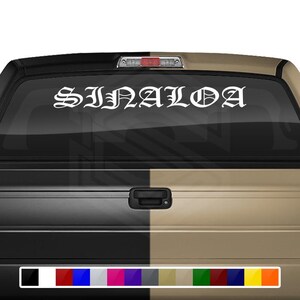 May include: White vinyl decal with the word "SINALOA" in a gothic font style. The decal is applied to the rear window of a black and tan pickup truck.