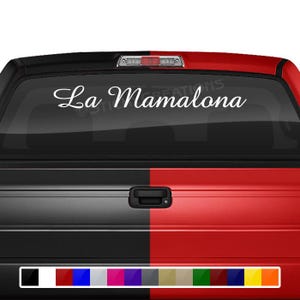 May include: A white truck with a black and red tailgate. The truck has a rear window with a white vinyl decal that says "La Mamalona".