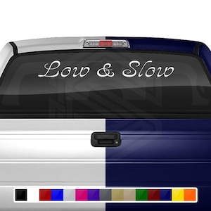 May include: White vinyl decal with the text "Low & Slow" in a cursive font. The decal is applied to the rear window of a pickup truck.
