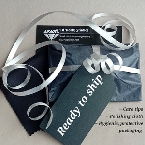 May include: A black and white gift box with a white ribbon and a black tag that says "Ready to ship". The box is wrapped in black tissue paper and has a small white card that says "Til Death Studios, Small batch & custom jewellery, Est. Halloween 2014".