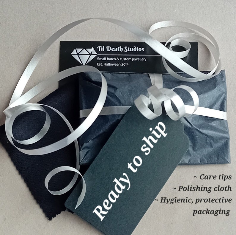 May include: A black and white gift box with a white ribbon and a black tag that says "Ready to ship". The box is wrapped in black tissue paper and has a small white card that says "Til Death Studios, Small batch & custom jewellery, Est. Halloween 2014".