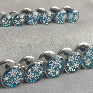 Steel silver toned double flared handcrafted ear gauges with blue resin, glitter accents and white snowflake designs.