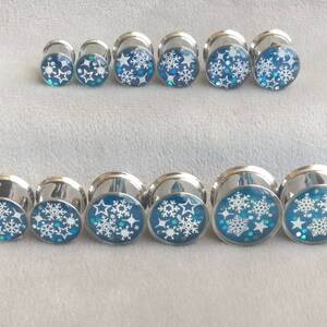 May include: A set of ten silver ear gauges with blue and white snowflake designs.
