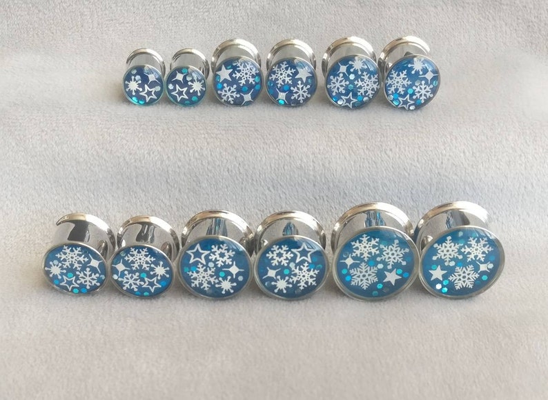 May include: A set of ten silver ear gauges with blue and white snowflake designs.