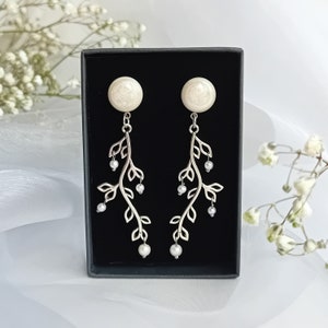 May include: A pair of silver earrings with a delicate branch design and white pearl accents. The earrings are displayed in a black box.