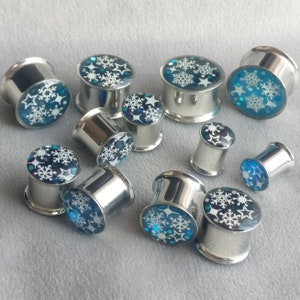 May include: A collection of silver metal ear gauges with blue and white snowflake designs.