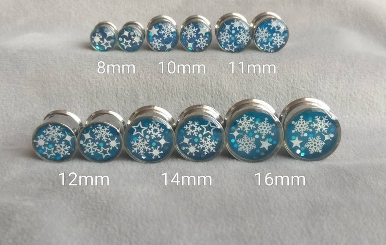 May include: Set of 10 silver ear gauges with blue and white snowflake designs. The gauges are 8mm, 10mm, 11mm, 12mm, 14mm, and 16mm in size.