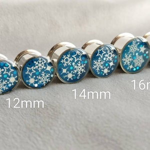 May include: Set of five silver ear gauges with blue and white snowflake designs. The gauges are 12mm, 14mm, 16mm in size.
