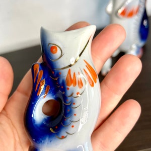 May include: A porcelain fish figurine with blue and white glaze and orange accents. The fish has a hole in the side, suggesting it may be a bottle stopper.