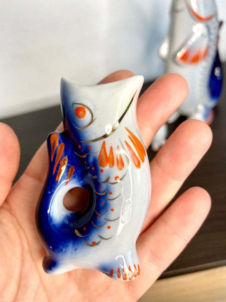 May include: A porcelain fish figurine with blue and white glaze and orange accents. The fish has a hole in the side, suggesting it may be a bottle stopper.