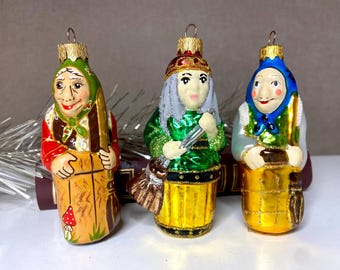 May include: Three hand-painted glass Christmas ornaments depicting whimsical figures. Each ornament features a unique design with vibrant colors, including red, green, and gold. The figures are dressed in traditional attire and hold various props, adding to their charm.