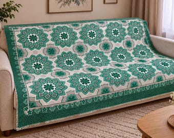 Peut inclure: Un plaid tissé rectangulaire présentant un motif répétitif de grandes fleurs mandala bleu sarcelle et vert foncé sur un fond gris clair, bordé d'une bordure vert foncé unie ornée d'un petit motif de fleurs blanches.