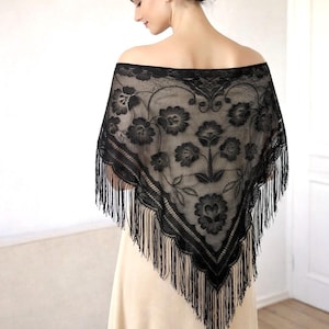 May include: Black lace shawl with a floral pattern and fringe trim. The shawl is draped over the shoulders, creating a triangular shape. The intricate design features detailed flower and leaf motifs.