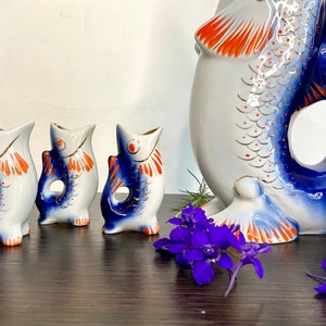 May include: Set of four blue and white porcelain fish-shaped shot glasses with orange and gold accents. The set includes a larger fish-shaped pitcher with a blue and white design.