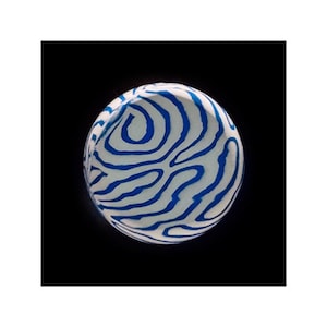 May include: A white sphere with a blue and white striped pattern. The sphere is against a black background.