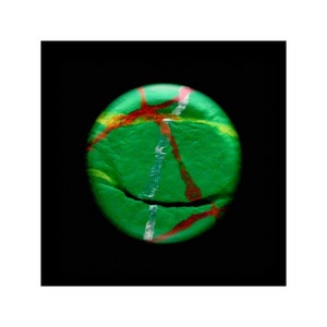 May include: A green ball with red, white, and yellow lines painted on it. The ball has a crack in it.