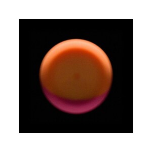 May include: A close-up of a round, orange and pink candle with a smooth, glossy finish.