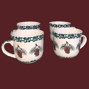 May include: A set of four white ceramic mugs featuring a repeating pattern of brown pinecones and green pine needles around the body. Each mug has a dark green decorative band around the rim and a sturdy handle on the side for easy gripping.