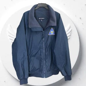 May include: Navy blue zip-up jacket with a fleece-lined collar. The jacket features a small patch with a blue, yellow, and white design. The brand name "PORT AUTHORITY" is visible on the collar. A practical and stylish outerwear option.