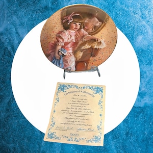 May include: A porcelain collector's plate featuring a painting of a young girl in a pink dress riding a rocking horse. The plate is decorated with a gold trim and has a certificate of authenticity.