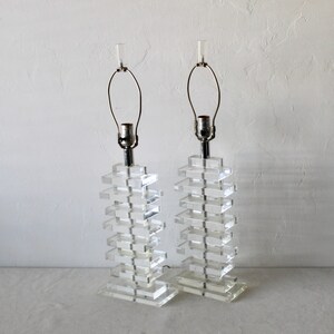 May include: A pair of clear acrylic table lamps with stacked rectangular bases and chrome accents. The lamps have a simple, modern design.