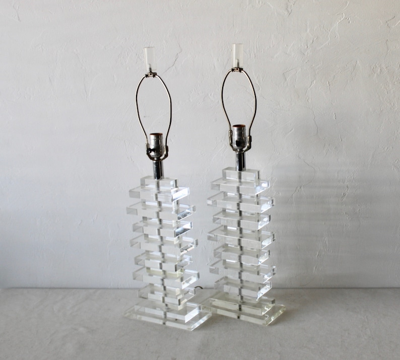 May include: A pair of clear acrylic table lamps with stacked rectangular bases and chrome accents. The lamps have a simple, modern design.