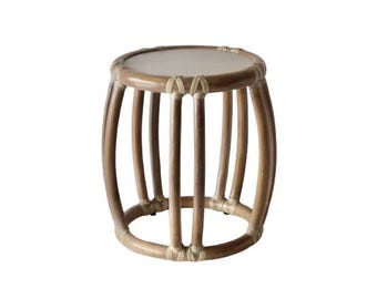 Pode incluir: Uma pequena mesa lateral redonda feita de rattan castanho claro. A mesa tem um tampo circular e uma série de suportes verticais curvos, conectados na parte superior e inferior. Os suportes são amarrados com barbante de cor natural.
