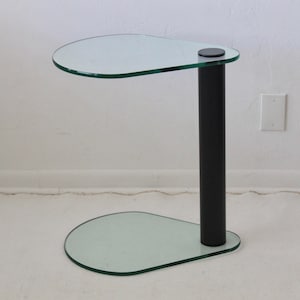 May include: A glass side table with a black metal base. The table top and base are shaped like an oval.