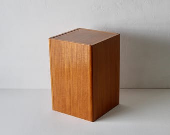 Pode incluir: Um armário de madeira retangular com acabamento castanho claro. O armário tem um design simples e minimalista com um tampo plano e um padrão de grão vertical suave. O armário é provavelmente usado para armazenamento.