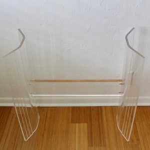 May include: A clear acrylic stool with a curved design and a single shelf. The stool is made of clear acrylic and has a modern design.