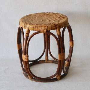 Puede incluir: Un taburete redondo de mimbre tejido con un acabado marrón natural. El taburete tiene una parte superior circular tejida y una base de mimbre tejido.