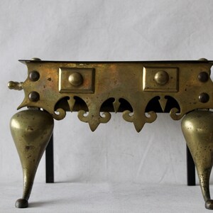 May include: A brass fireplace stand with three legs and a decorative top. The stand has a black metal frame and ornate details.