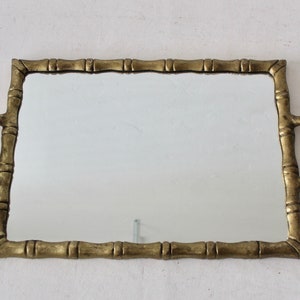 May include: A gold-toned rectangular tray with bamboo-style handles and a mirrored surface.