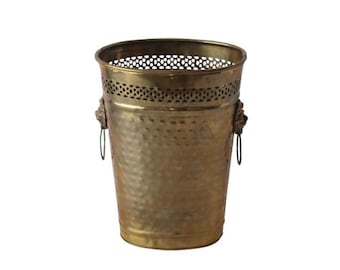 Pode incluir: Um balde de metal dourado com textura martelada. A borda superior tem um design perfurado decorativo. Alças de cabeça de leão com argolas em ambos os lados. O balde é um item decorativo.