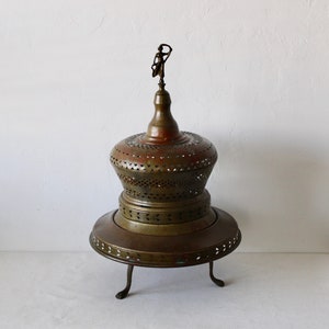 Può includere: Un bruciatore di incenso in piedi in ottone e rame con un design traforato decorativo e una piccola figura in cima.