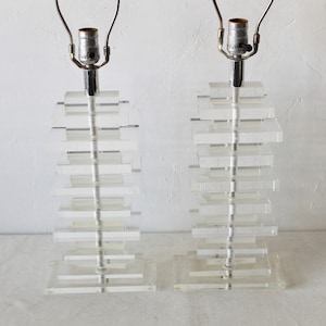 May include: Two clear acrylic lamps with a stacked design. Each lamp has a silver metal base and a clear glass shade.