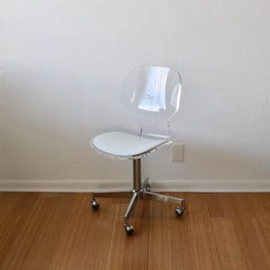 May include: A clear acrylic office chair with a white padded seat and chrome base with five wheels.