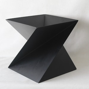 May include: A black metal geometric planter with a square base and a twisted, angular design.