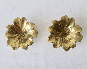 Pode incluir: Duas travessas decorativas douradas em forma de folha. As travessas apresentam veios detalhados e uma forma ligeiramente côncava. As folhas estão dispostas lado a lado sobre um fundo branco. Podem ser usadas como tigelas ou bandejas decorativas.