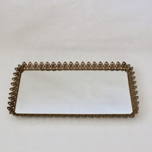 May include: A gold-colored metal tray with a decorative, scalloped edge and a mirrored surface.