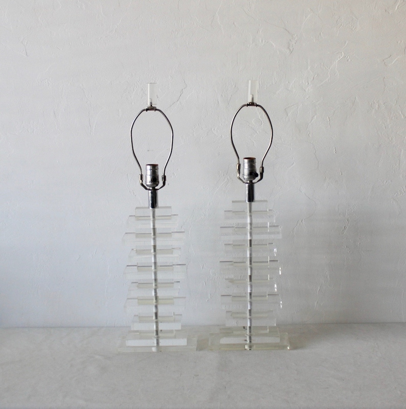 May include: A pair of clear acrylic table lamps with stacked rectangular bases and chrome lampshades.
