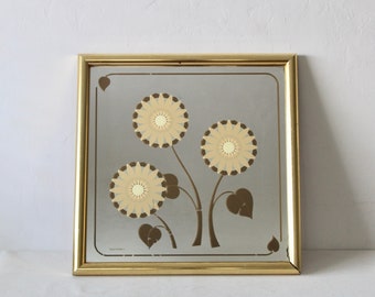 Pode incluir: Um espelho com moldura dourada com um design floral. O espelho tem um fundo castanho claro com três flores estilizadas em tons de amarelo e castanho.