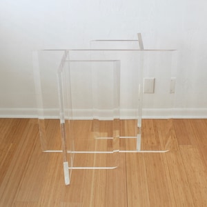 May include: A clear acrylic table base with four legs. The base is made of multiple pieces of acrylic that are stacked and joined together.