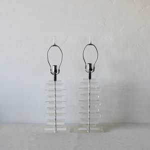 May include: A pair of clear acrylic table lamps with a stacked design. Each lamp has a simple metal base and a clear glass shade.
