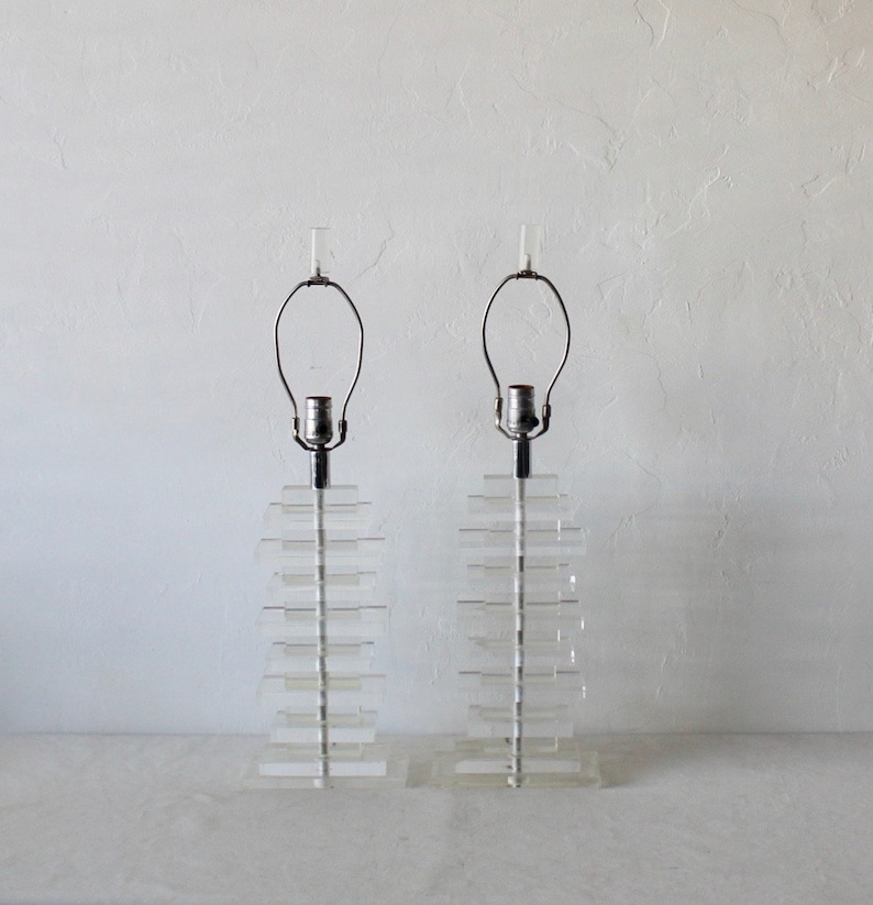 May include: A pair of clear acrylic table lamps with a stacked design. Each lamp has a simple metal base and a clear glass shade.