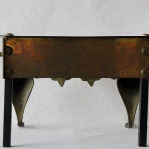 May include: A vintage brass and black metal fireplace stand with a rectangular top and four legs. The stand has a decorative design on the front and back.
