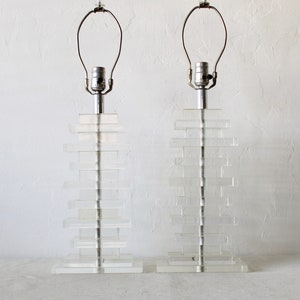 May include: A pair of clear acrylic table lamps with stacked rectangular bases and silver metal lampshades.