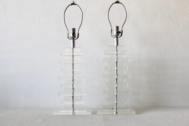 May include: A pair of clear acrylic table lamps with stacked rectangular bases and silver metal lampshades.